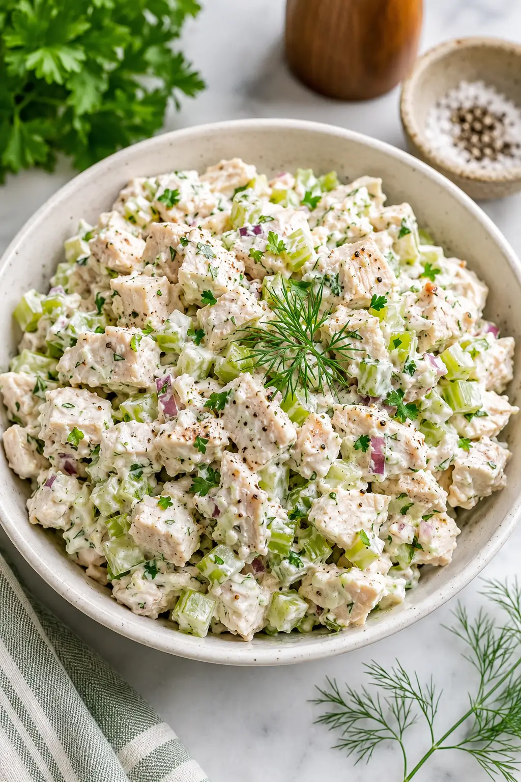 Creamy chicken salad with celery, parsley and chives in a white bowl.