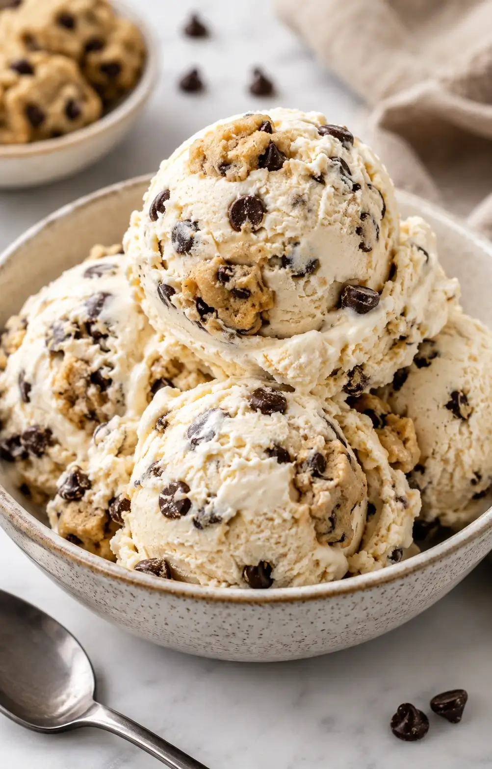 Scoops of cookie dough ice cream with visible chocolate-chip cookie dough pieces in a white bowl.
