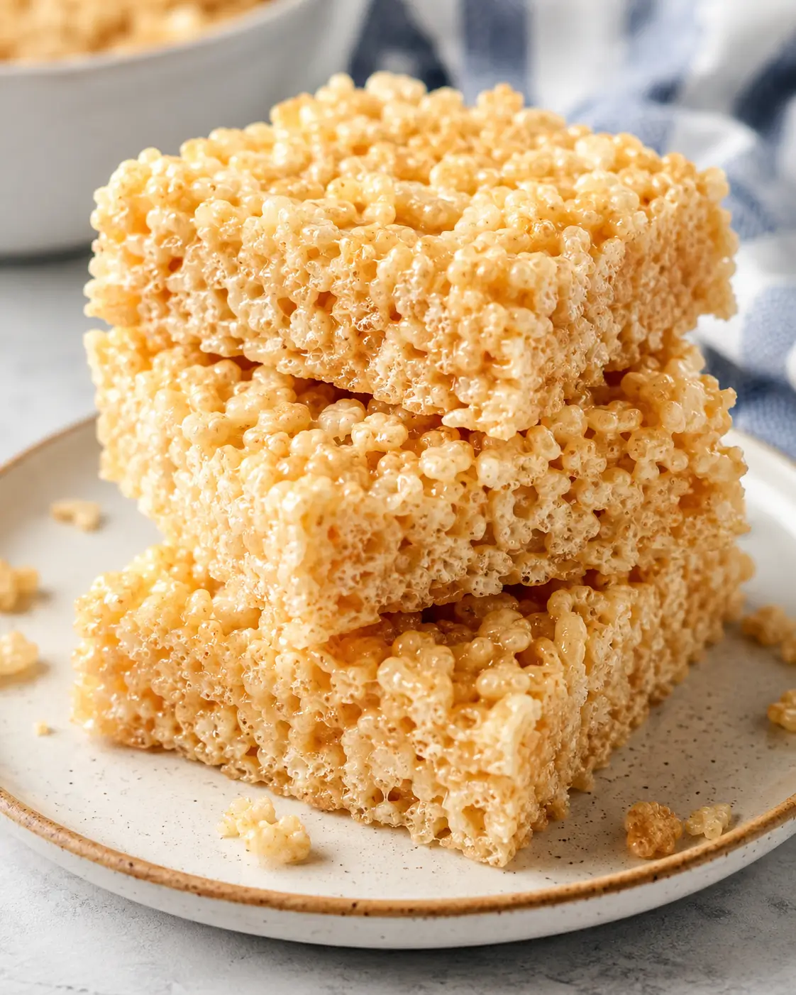 Classic Rice Krispie treats cut into squares and stacked on a white plate.