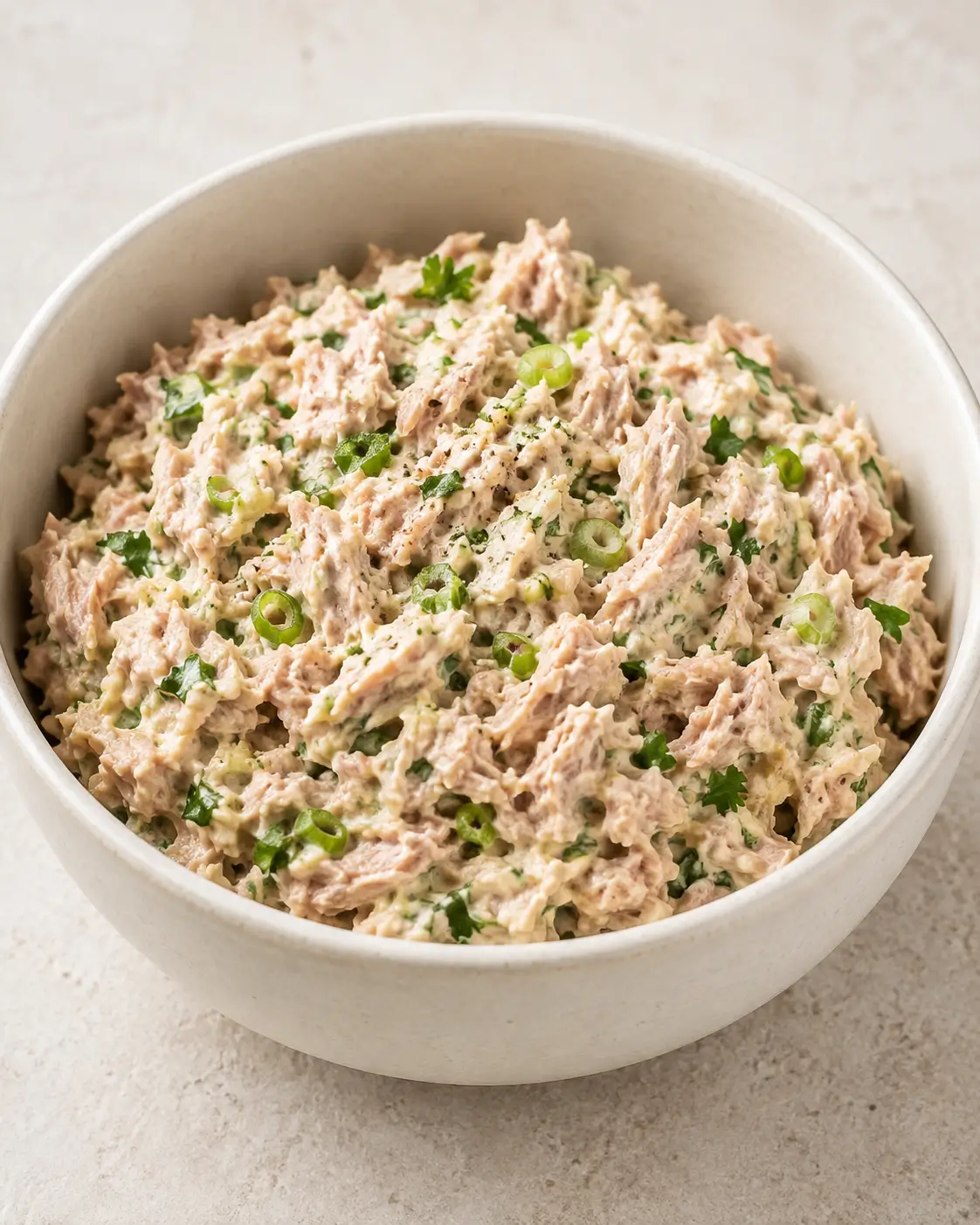Classic tuna salad with green onions and parsley in a white bowl.